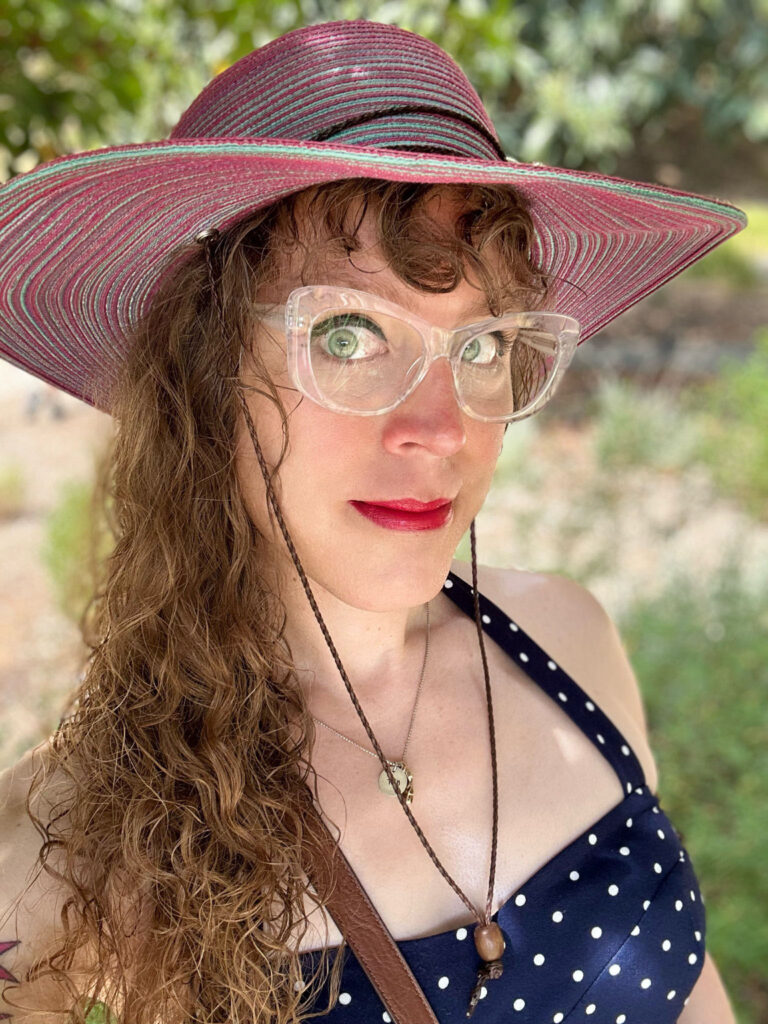 Me outside in a blue and white polka-dot halter top and my stealth trans-pride colors sun hat