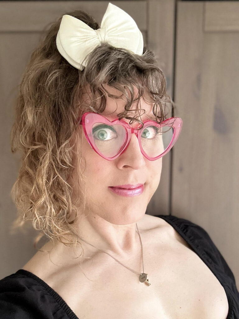 Me with my hair up in a pineapple held with a large white bow, in a black top with as close to cleavage as my body will allow and pink heart-shaped glasses.