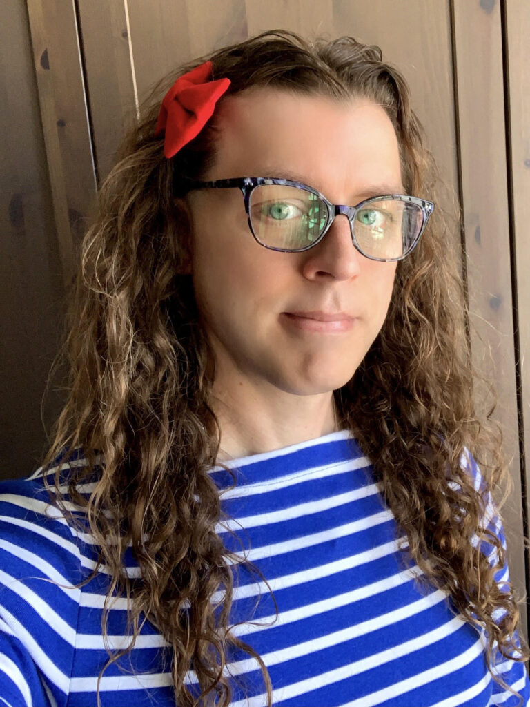 Me in a blue and white horizontal striped shirt, with my long brown curly hair (no curly bangs yet), and my childhood red bow in my hair.