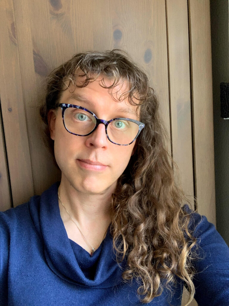 Me with short and odd curly bangs and long brown curly hair. My eyes look a little more lively but it still feels off to me.