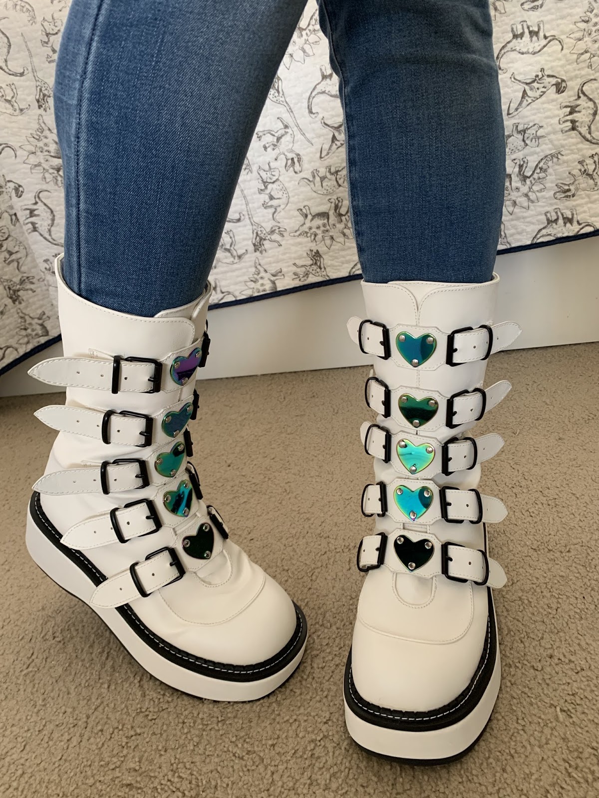 Me wearing a pair of white platform boots that have four buckles up the front, and the center of each buckle is an iridescent metal heart.