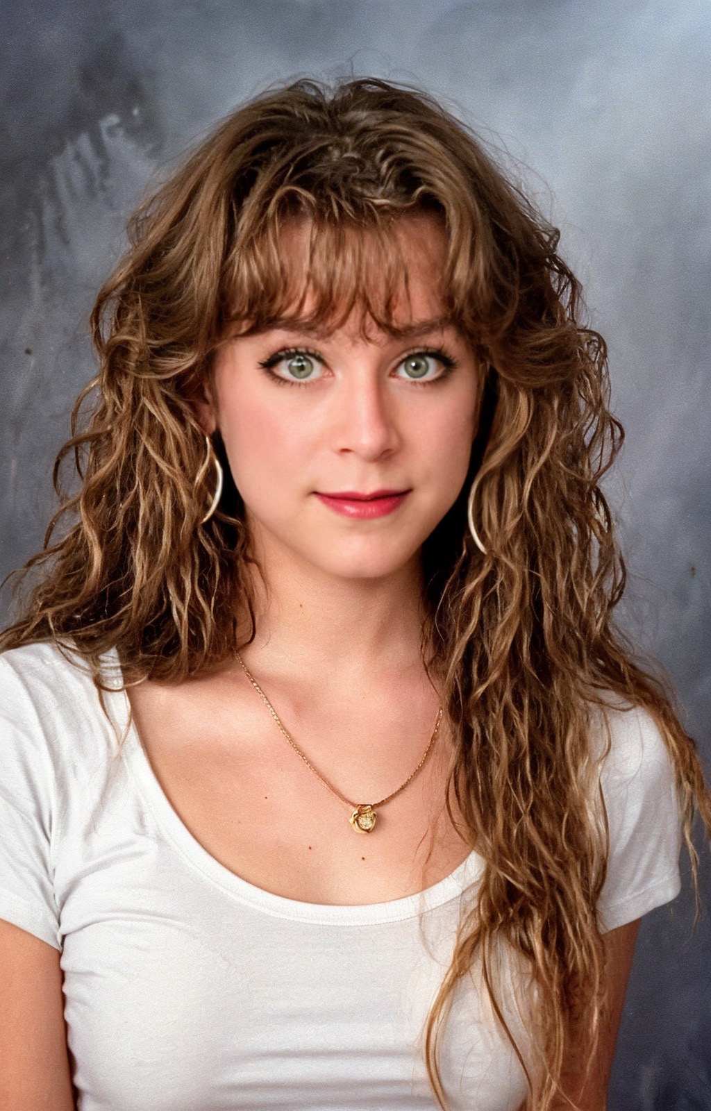 Older teen Tilly with long brown wavy hair and bangs, in a white t-shirt.