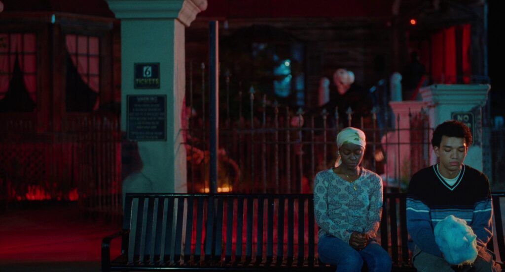 Owen and his mom, all in blue, sitting on a blue bench, with Owen holding blue cotton candy. There is a bright red light behind them.