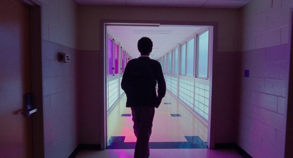 Owen walks down a hallway where all the windows on the left are pink, and all the windows on the right are blue. 