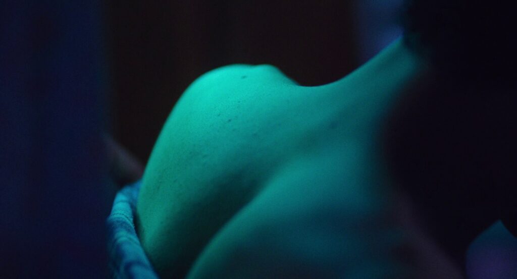 A shot of Owen’s bare shoulders and neck bathed in green light.