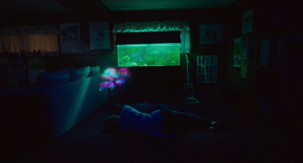 Owen sleeping under the green fishtank, tv static hovers in the air over his head in pink, blue, and green.