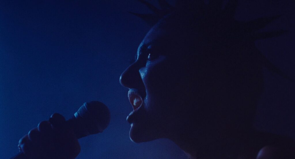 King Woman singing, entirely in blue light.