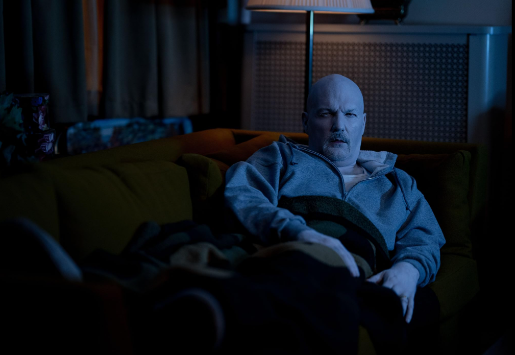 Owen’s dad lying on a couch, bathed in blue light, with yellow light behind him.