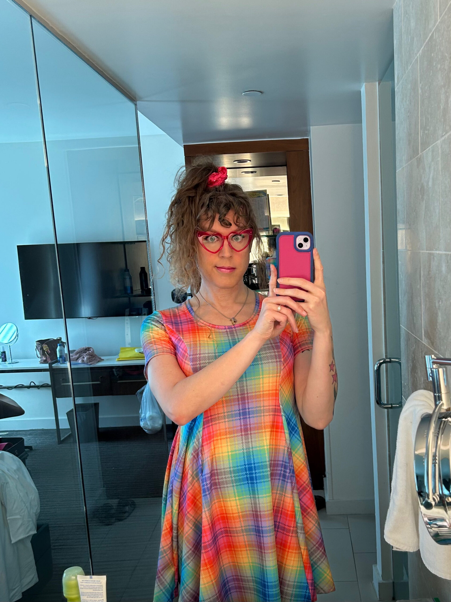 Me in a rainbow plaid dress with my long brown curly hair up in a pineapple, taking a mirror selfie