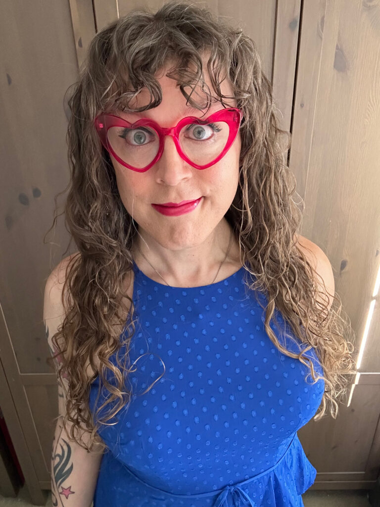 A straight-on shot of me in a blue dress and pink heart-shaped glasses.