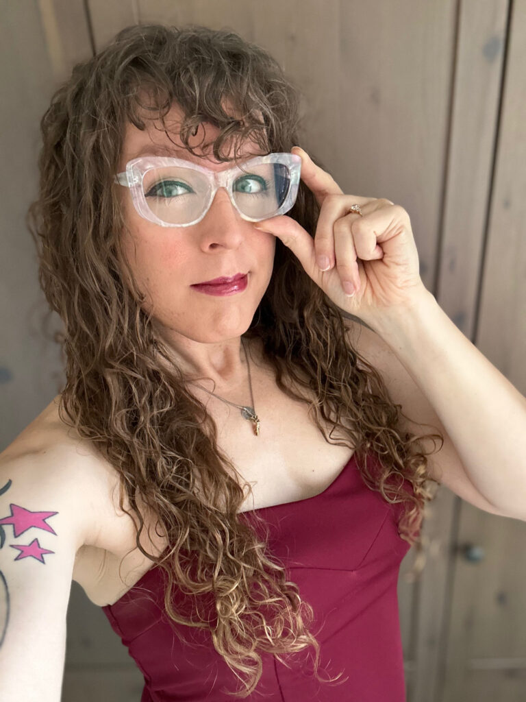 Me in a red halter top and white iridescent cat eye glasses. I’m adjusting the glasses and squinting suspiciously.